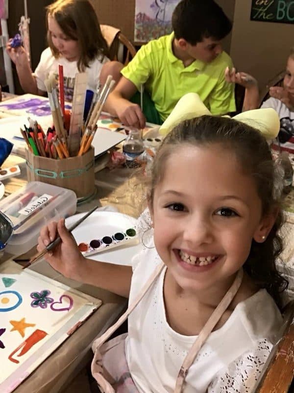 A girl grinning over her paint palette